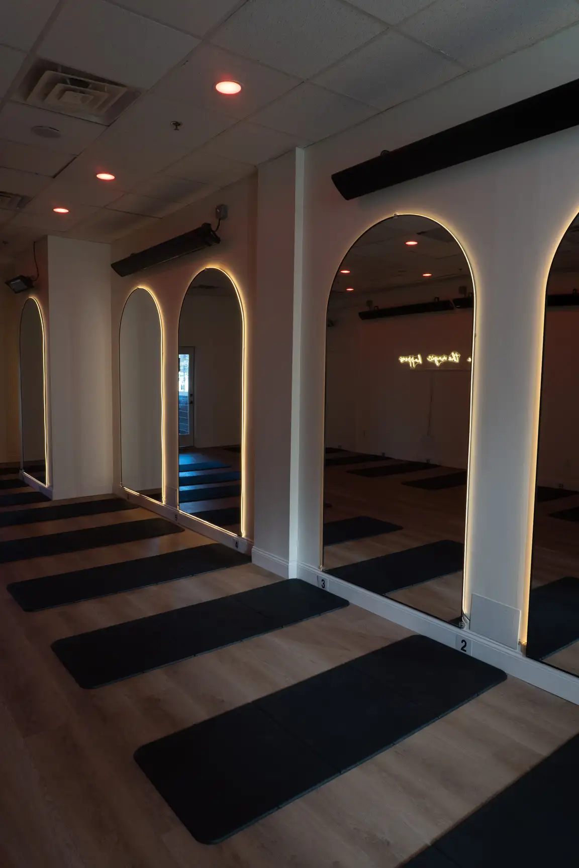 Empty COREFLOW studio with backlit arched mirrors, infrared heaters and mats laid out on a wood floor