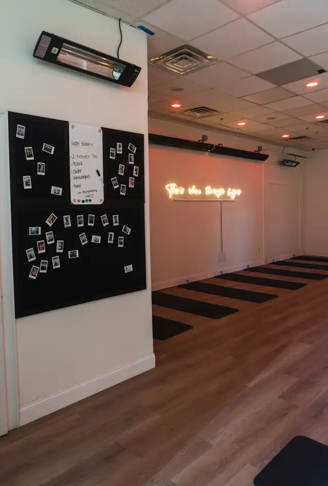 The COREFLOW studio floor with mats in place, an infrared heater overhead and the neon sign lit on the far wall